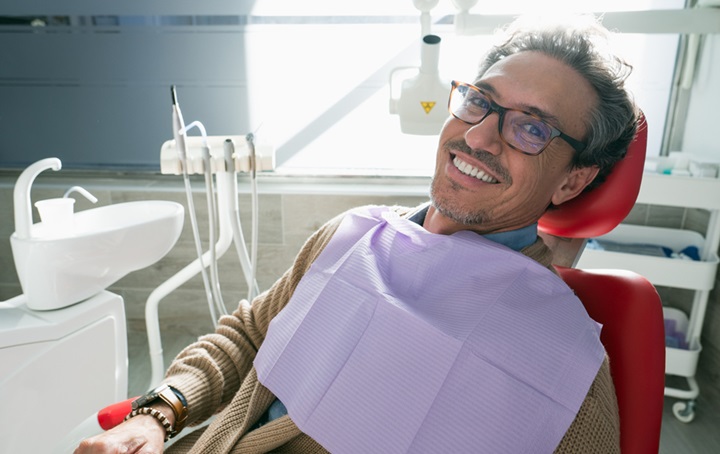An image of a male, smiling while sitting in a dentist chair